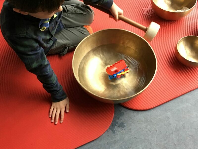 Klangpädagogik im Schulkontext Kind spielt mit wassergefüllter Klangschale auf dem Boden