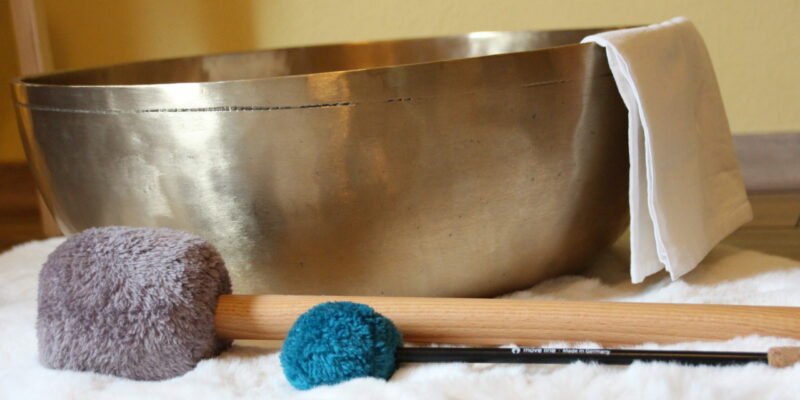 Klangschale auf Fell, zwei Schlegel (grau und türkis) daneben, Tuch an der Seite