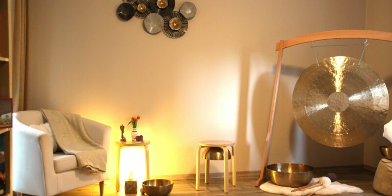 Einladender Raum mit Sessel, Klangschalen, halbem Gong, Hocker, Tisch mit Blumen und dekorativer Wandgestaltung