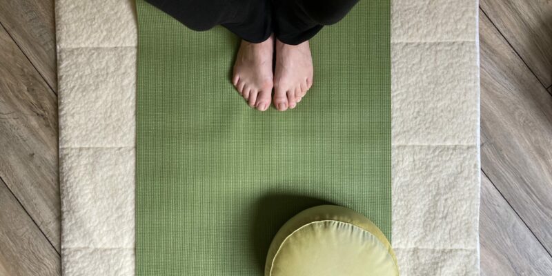 Füße auf grüner Yogamatte mit Wollmatte, Yogakissen und Holzfußboden