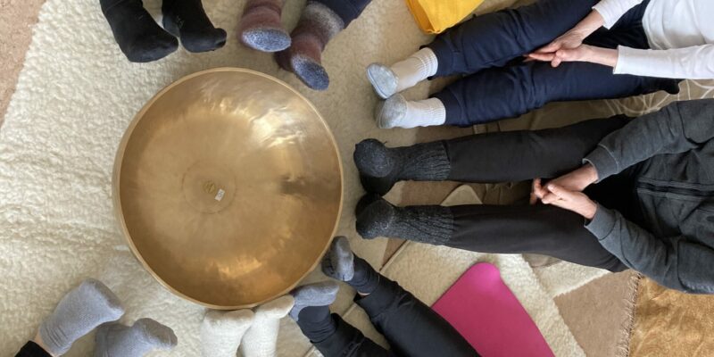 Klangraum in Gemeinschaft erleben Große goldene Klangschale mit Menschen in Sportkleidung sitzend im Kreis um die Klangschale