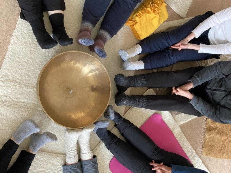 Klangraum in Gemeinschaft erleben Große goldene Klangschale mit Menschen in Sportkleidung sitzend im Kreis um die Klangschale