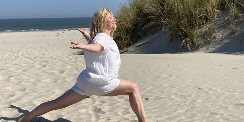 Kalenderabschluss – Yoga, Bewegung und Achtsamkeit auf wohlfuehlzeit-verl.de Frau in Yoga-Pose mit großem Ausfallschritt und seitlich ausgebreiteten Armen, Strand, Düne und Meer im Hintergrund
