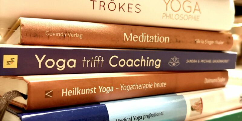 Stapel von Fachbüchern zu Yoga, Spiraldynamik, Coaching, Meditation, Resilienz und Peter Hess Klangmethoden mit bunten Buchrücken.