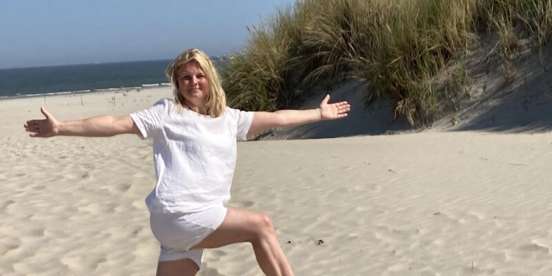 Mein Weg – der Beginn mit Yoga Frau in einer Yoga-Position am Strand mit ausgebreiteten Armen, Meer und Dünen im Hintergrund als Symbol für den Beginn des Yoga-Weges.