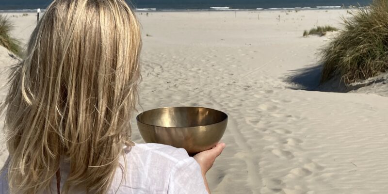 Klang und Weite am Meer Frau am Strand mit Klangschale in der Hand blickt Richtung Meer und Horizont