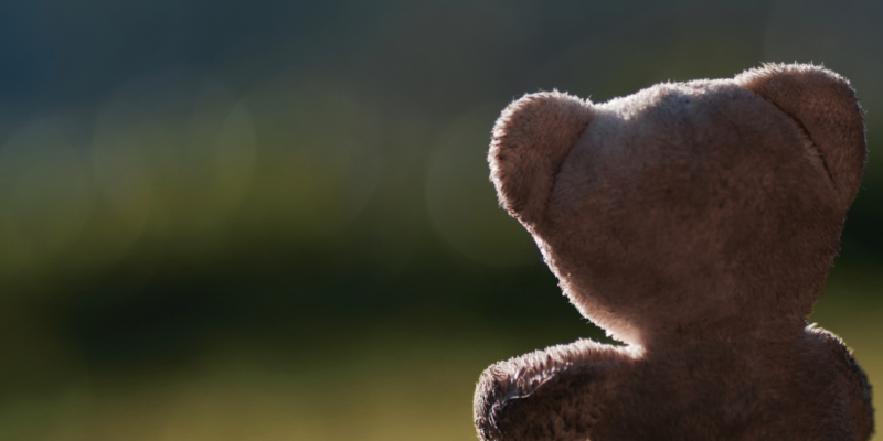 Ein sicherer Ort – Klangbasierte Trauerbegleitung für Kinder und Jugendliche Teddybär von hinten vor unscharfem, dunklerem Hintergrund als Symbol für kindliche Trauer und geschützte, klangbasierte Begleitung.