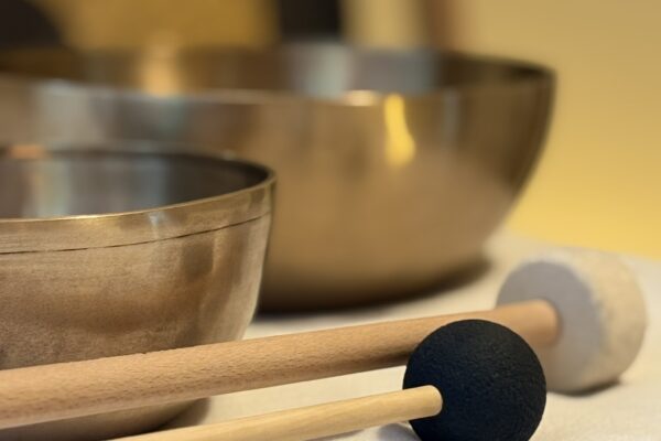 Klangschalen mit Schlegeln und Gong in Verl Zwei Klangschalen auf weißer Unterlage, davor zwei Schlegel mit Holzgriff (schwarze Kugel und weißer Filzring), im Hintergrund schemenhaft ein Tam-Tam-Gong.