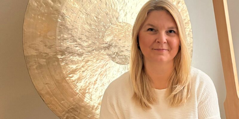 Frau schaut in die Kamera, hinter ihr ein goldener Gong in der Praxis