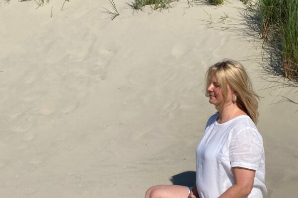 Innehalten und sich innerlich ausrichten für Achtsamkeit und Bewusstheit Frau Meditiert in einer Sanddühne bei Sonnenschein