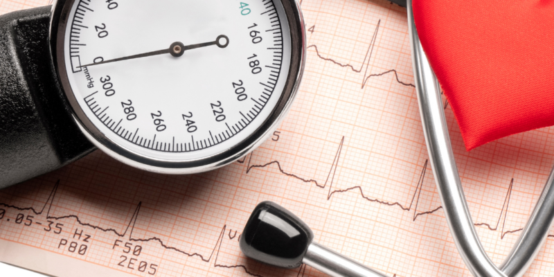 Blutdruckmessgerät mit Anzeige, EKG-Streifen und rotem Herz als Symbol für Meditation und Gesundheit